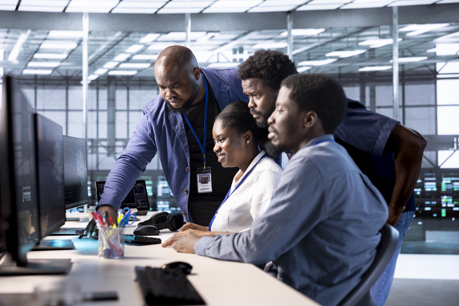 Four technicians collaborate around monitors in a bright server room.
